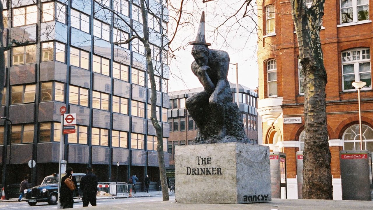 statuja-me-firmen-e-banksyt-shfaqet-ne-londer-vepra-misterioze-paraqet-nje-burre-me-flamur-qe-i-mbulon-fytyren